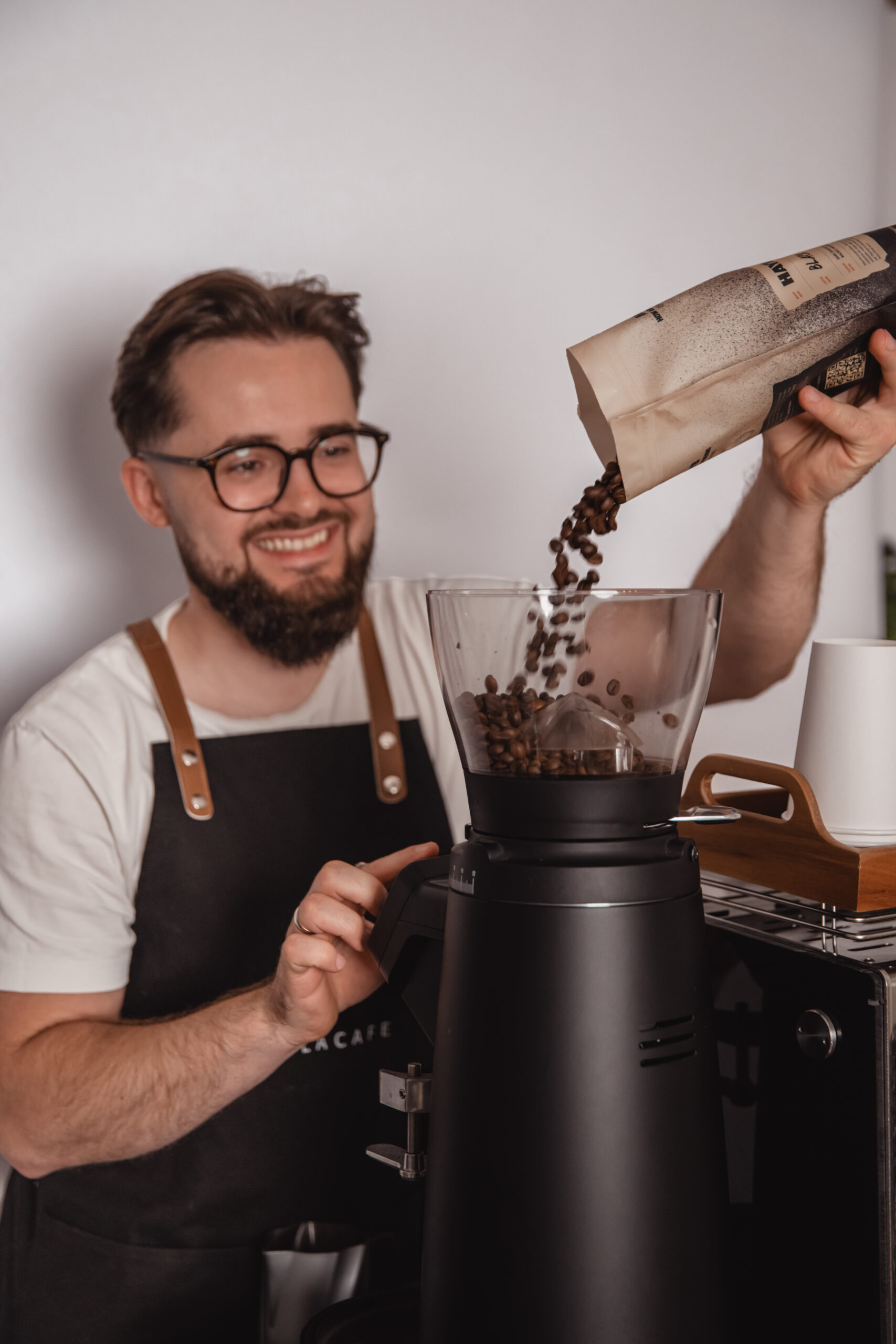 Barista Topola Café sypie kawę do młynka Compak i3 pro, w tle coffee cart